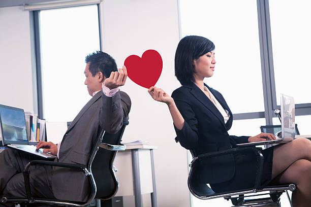 Work romance between two business people holding a heart Work romance between two business people holding a heart flirty stock pictures, royalty-free photos & images