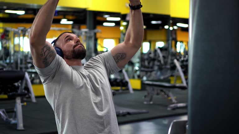 Young Man Lifting Weights And Listening To Music On Headphones In The Gym