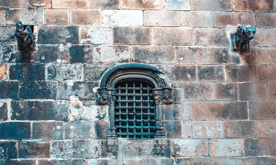 Old grilled window in brick stone wall of castle photo. Urban scenery photography with fortress side wall. Gothic Quarter street scene in Catalonia, Spain. High quality picture for wallpaper, article