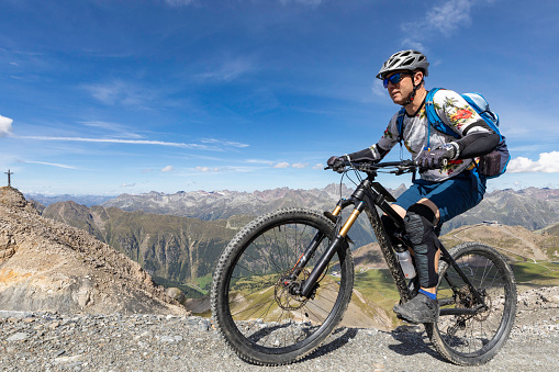 A well equipped male mountainbiker is taking a steep ride uphill towards the summit on a sunny summer day at the scenic Engadin Alps, Switzerland.\nCanon EOS 5D Mark IV, 1/1000, f/8, 16 mm.