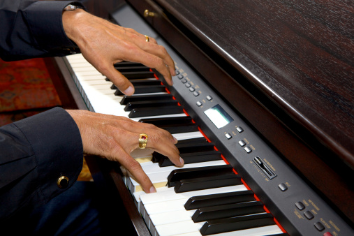 The hands of an older Indian male on the keyboard of a digital piano.  Good finger position.  The left hand comes off the keyboard in a Rest.  The darker skin makes a good contrast against the white of the keyboard.  The control buttons of the piano can be seen