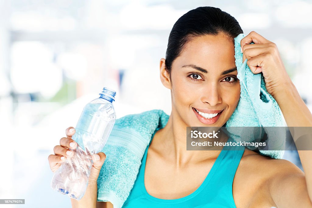 Woman Holding Bottle While Cleaning Sweat From Forehead In Gym Portrait of confident young woman holding water bottle while cleaning sweat from forehead after intense workout in gym. Horizontal shot. 20-24 Years Stock Photo