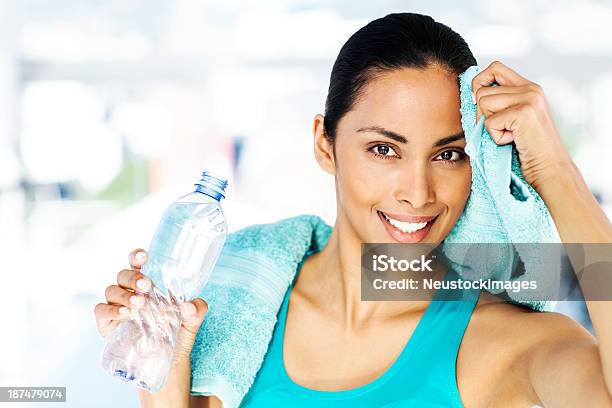 Woman Holding Bottle While Cleaning Sweat From Forehead In Gym Stock Photo - Download Image Now