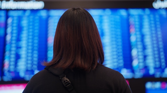 An Asian female tourist is checking for the flight information at airport.