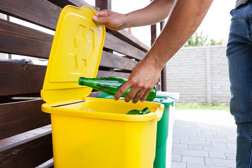 Man throwing the glass bottle into one of three dustbins for sorting trash