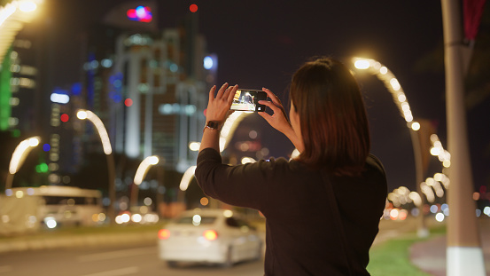 An Asian female traveler is taking photos and videos with her mobile smart phone in Doha, Qatar.