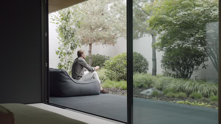 Man sitting on comfortable bean bag chair on terrace and drink coffee