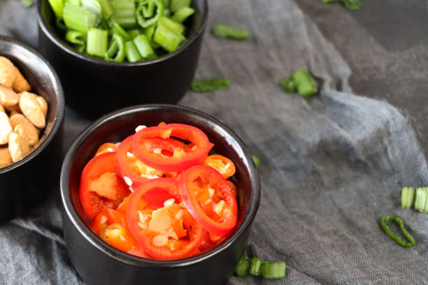 istock Close-up image of three black ramekins containing chopped red chilli, peanuts and spring onion, grey muslin background, elevated view, focus on foreground 1874845654