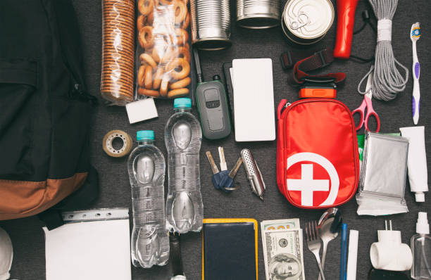istock Emergency backpack equipment organized on the table. Documents, water,food, first aid kit and another items needed to survive. 1874855402