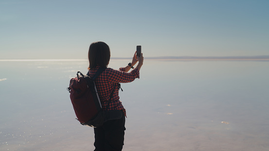 An Asian female tourist is using her mobile smart phone to take photos  and videos in salt lake in Turkiye, Turkey.