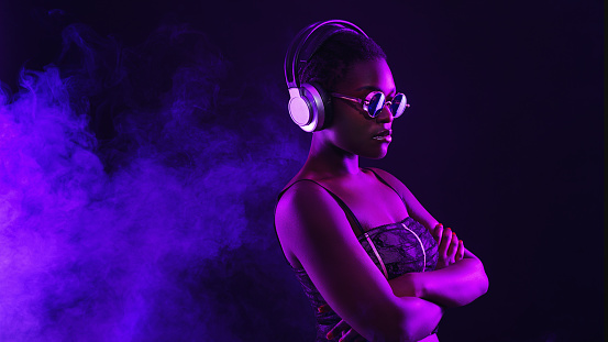 Portrait of fashion young girl in cool sunglasses and with headphones in red and blue neon light in the studio.