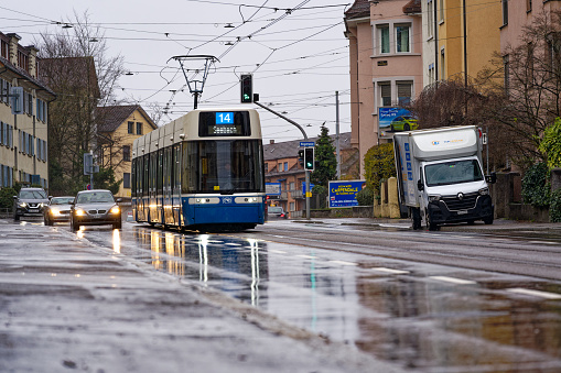 Diminishing view of blue and white tram lien 14 direction Seebach on a wet road at Swiss City of Zürich on a winter day. Photo taken December 22nd, 2023, Zurich, Switzerland.