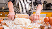 Woman confectioner in a striped culinary apron rolls the dough while making homemade baking, close up