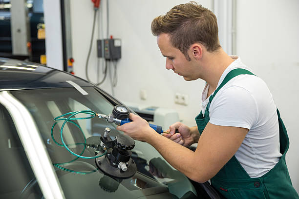 istock Man in green apron repairing damage on car windshield 187490432