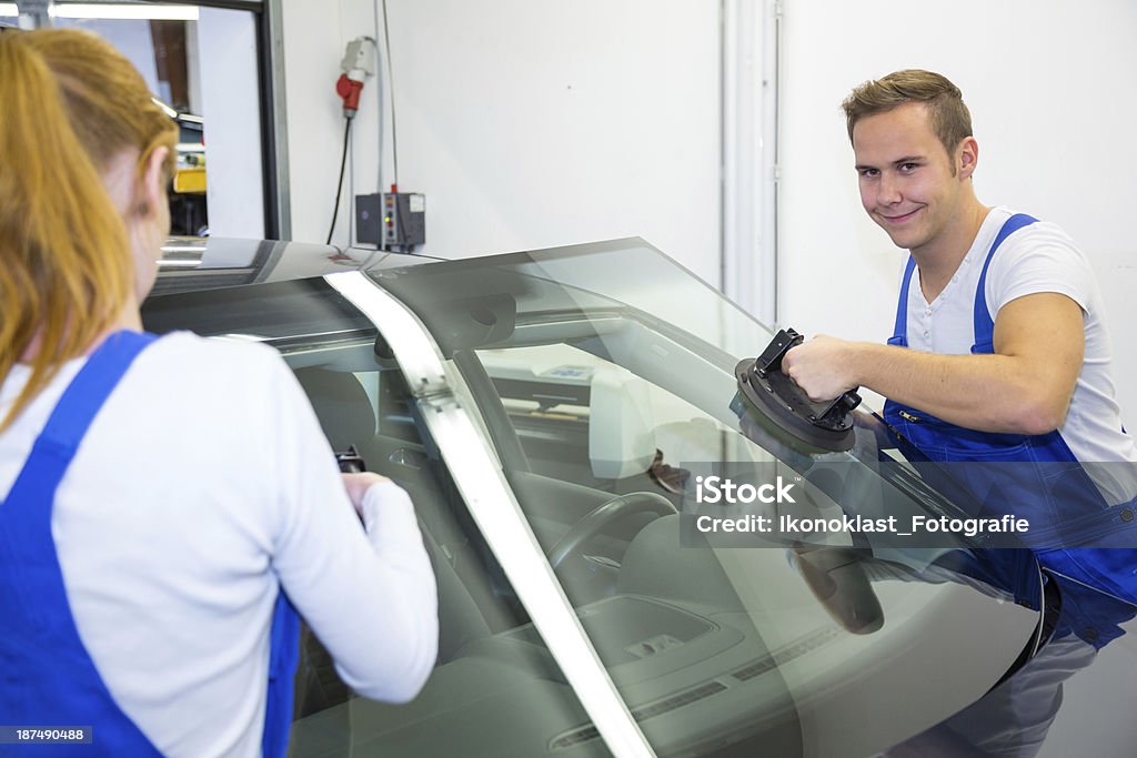 Two glaziers in garage replace windshield or windscreen on car Windshield or windscreen replacement on a car by couple of glaziers in garage Gestational Surrogacy Stock Photo