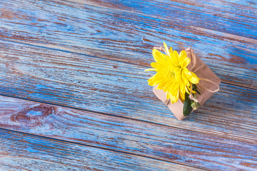 Top view of gift decorated with yellow chrysanthemum flower and space for greeting text, flat lay. Still life on a wooden background