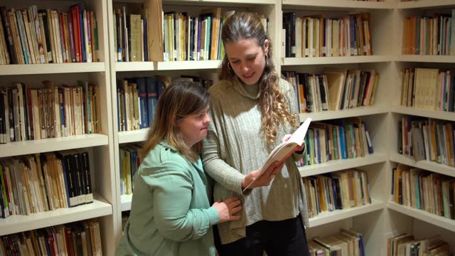 Mid adult woman with special needs reading a book with teacher in the library