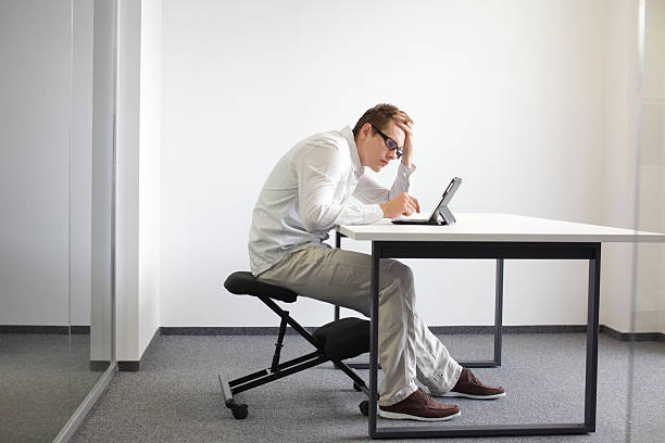 man is bent over  tablet.Bad sitting posture at work stock photo