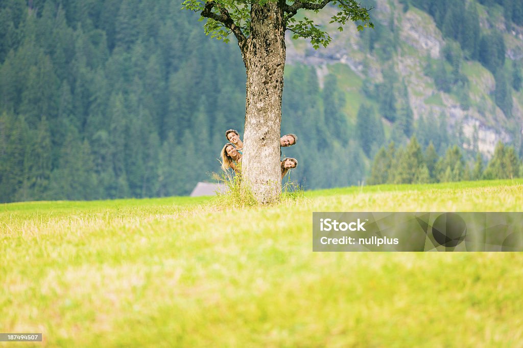 Famiglia di quattro nascondersi dietro albero - Foto stock royalty-free di Bambino