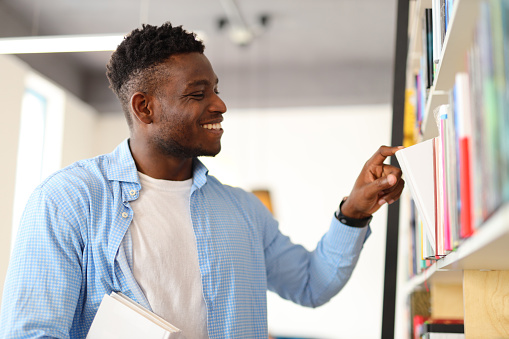 A dedicated college student in a library, focused on selecting and studying books for academic pursuits.