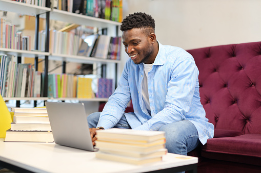 A happy and focused student utilizing a laptop for studying and research in a modern library setting.