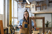 Portrait of young female carpenter using mobile phone in her workshop