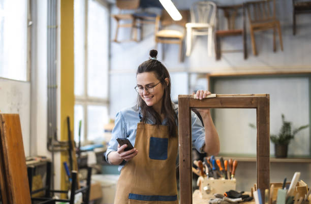 istock Portrait of young female carpenter using mobile phone in her workshop 1874961764