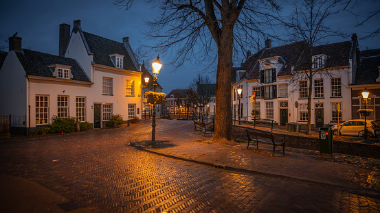 Empty cobblestone city street, surrounded by historic medieval buildings in the old town of Amersfoort. Illuminated street lights at dawn. Holland in the Netherlands, Europe.