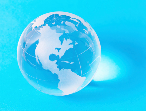 A glass globe-shaped paperweight on a blue background with The Americas continent uppermost. Copy space on blue.