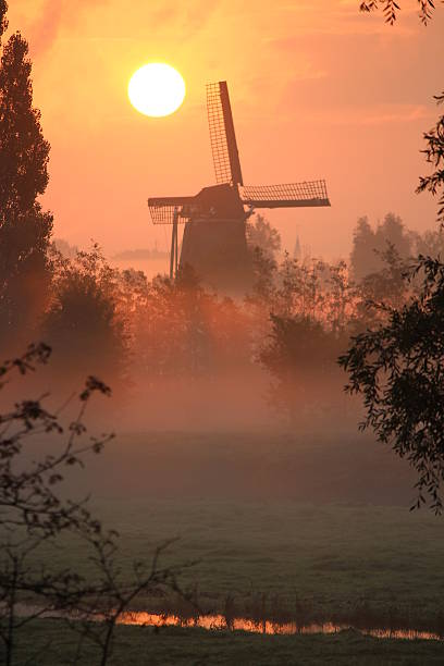 istock Windmill with the rising sun over a misty meadow 187498384