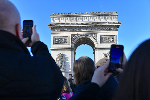 Paris, France-12 16 2023: Group of tourists using mobile phone photographing the Arc de Triomphe on the avenue des Champs-Elysées in Paris, France.