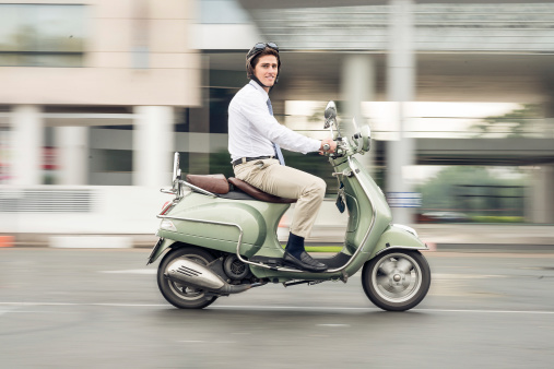 Image of a young businessman going at work on the scooter