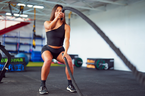 latin american woman doing battle ropes in the gym