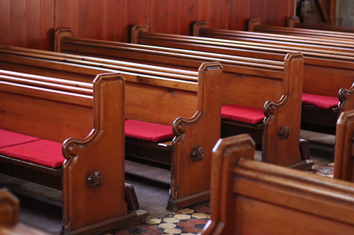 Rows of wooden church pews with Holy Bible and hymnal