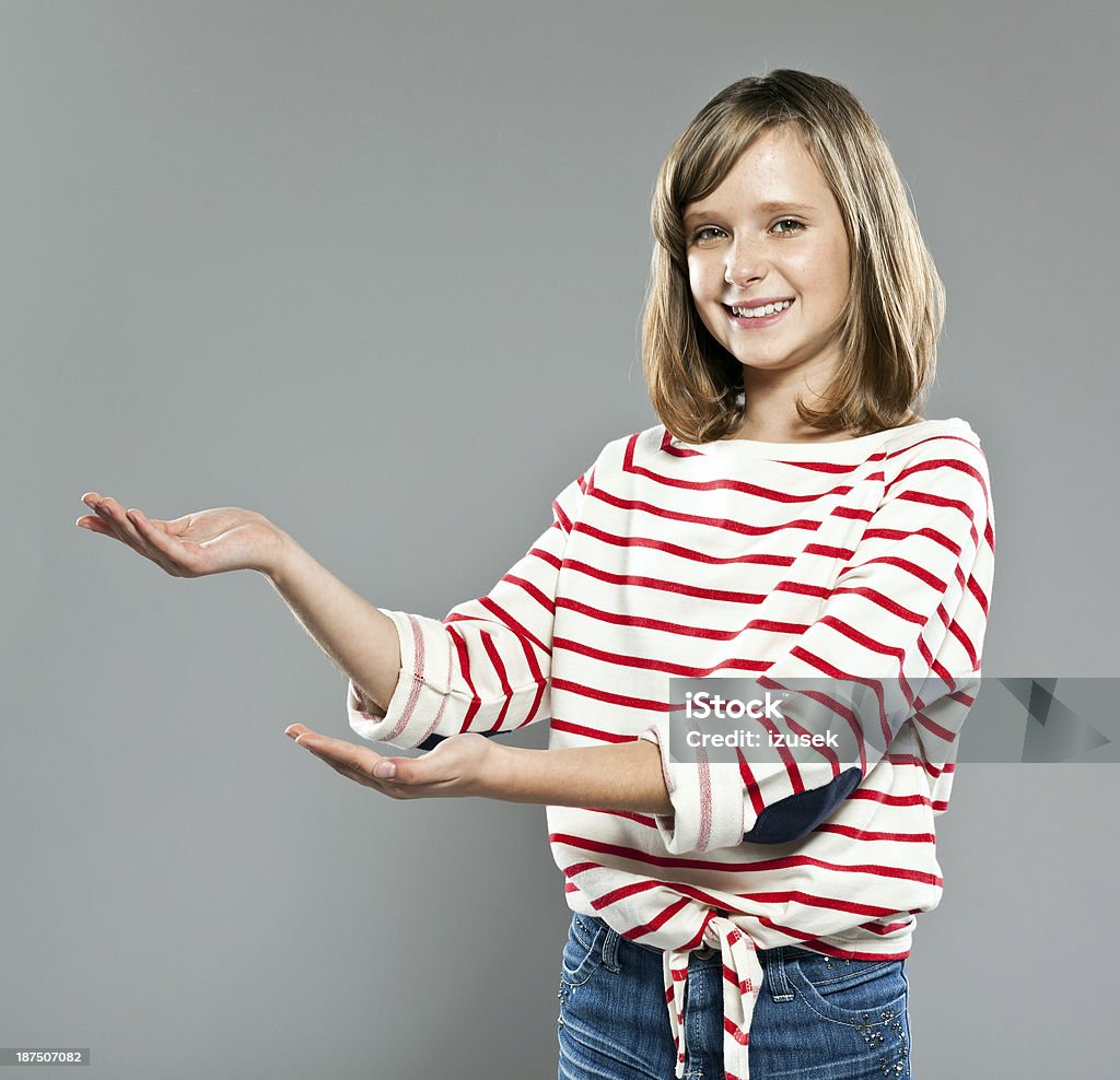 Schoolgirl pointing Portrait of cute girl wearing striped blouse and jeans, standing against grey background and pointing with hands, smiling at camera. 10-11 Years Stock Photo