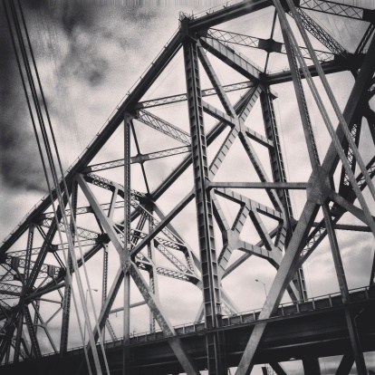 A moody black & white shot of the old Bay Bridge, with the cables of the new Bay Bridge in the foreground.  Taken with an iPhone and processed in Instagram.