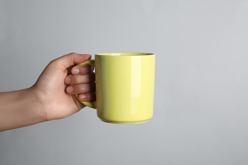 Woman holding yellow mug on light grey background, closeup