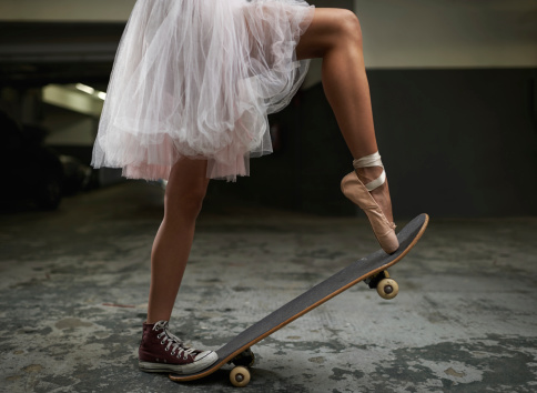 A cropped image of a woman on a skateboard wearing one sneakers and a ballet slipper