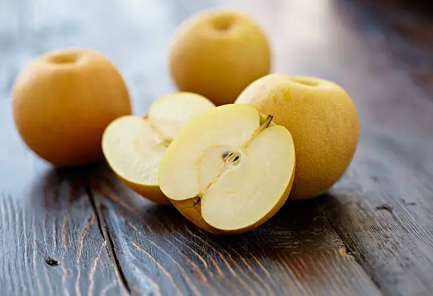 Asian pear sliced and three whole pears shot on wood background with shallow depth of focus.  Professionally shot, color corrected, exported 16 bit and retouched for maximum image quality.