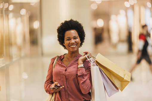 Portrait of a very happy Black woman holding bags and looking at camera while enjoying a day of shopping in the city mall.