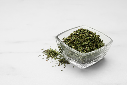 Dry tarragon in glass bowl on white table, space for text