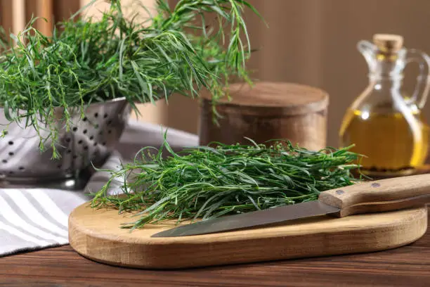 Board with fresh tarragon leaves and knife on wooden table