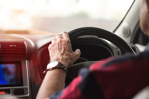 close-up of an adult man's hand holding the steering wheel of a car while driving