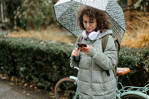 Businesswoman on the rain, commuting to work and using a mobile phone