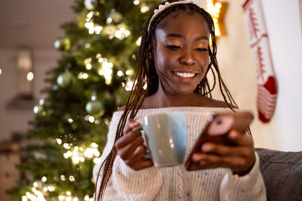 istock Woman Black ethnicity enjoying Christmas atmosphere, while drinking hot chocolate and using mobile phone 1875181617