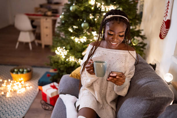 istock Woman Black ethnicity enjoying Christmas atmosphere, while drinking hot chocolate and using mobile phone 1875183157