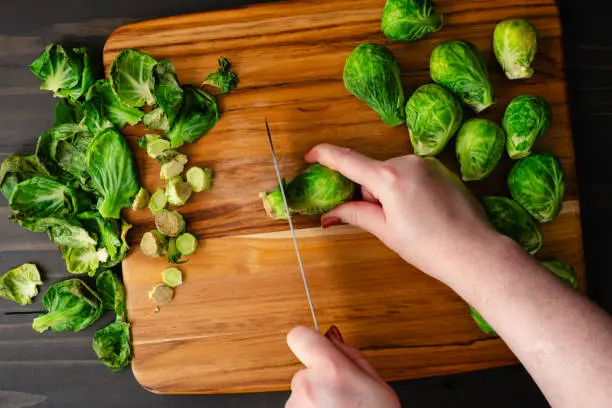 Chef's hands peeling and trimming raw baby cabbages on a wooden cutting board