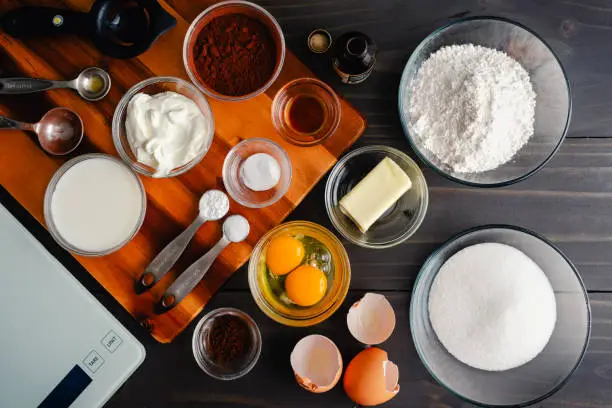 Overhead view of cake ingredients in prep bowls with measuring spoons, egg separator, and scale