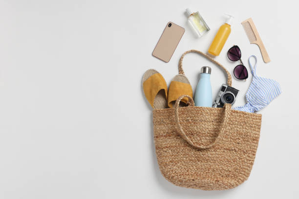 Wicker bag, smartphone and beach accessories on white background, flat lay. Space for text