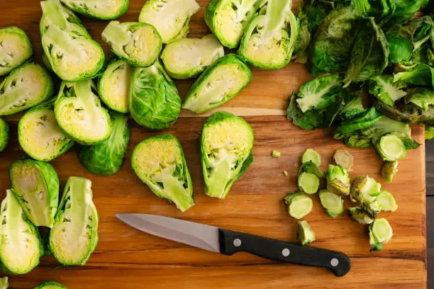 Fresh brussels sprouts halved with a paring knife on a wooden carving board